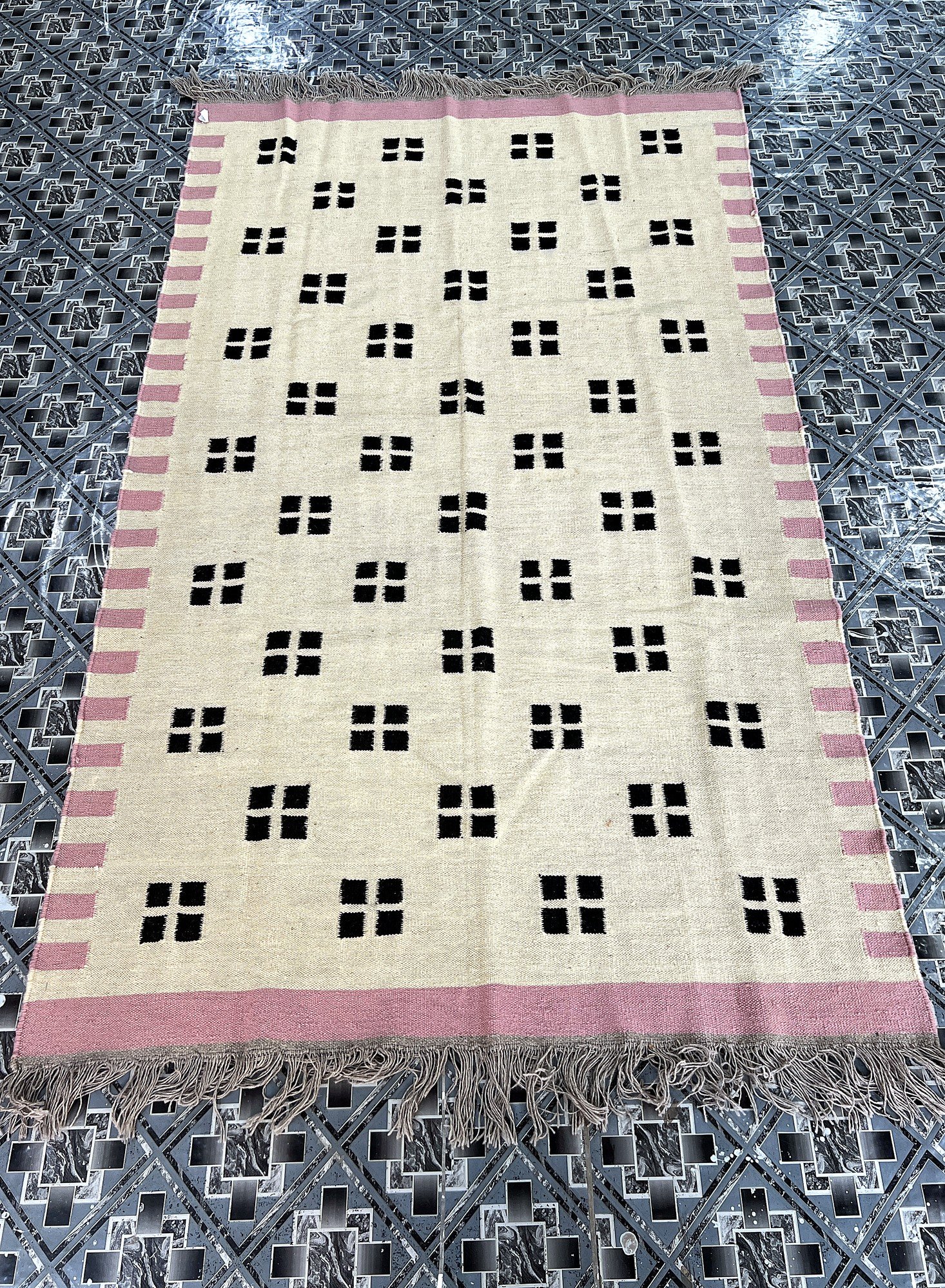 Angled full-length view of the handwoven ivory kilim rug with black confetti dot pattern and pink border | The Rugs Curator — Pakistani Premium Rugs