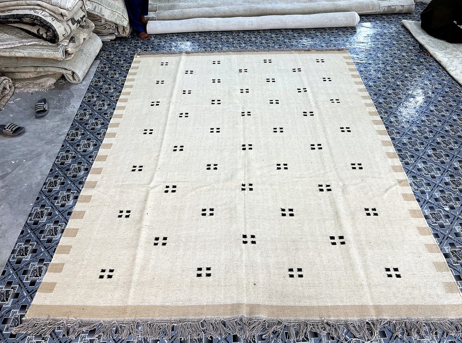 Angled full-length view of the handwoven ivory kilim rug with scattered black square-dot pattern, shown with fringe edge | The Rugs Curator — Pakistani Premium Rugs
